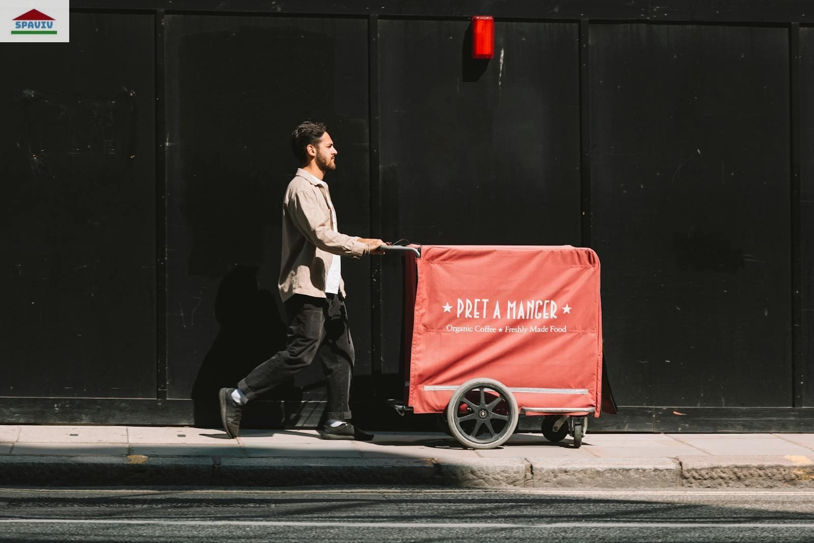 Man on a Street Pushing a Red Cart against a Black Wall