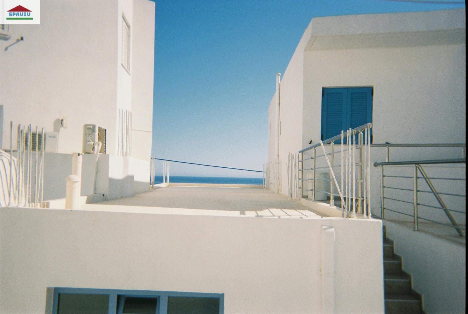 Minimalist white buildings with blue accents overlooking the sea, featuring rooftops and stairs.