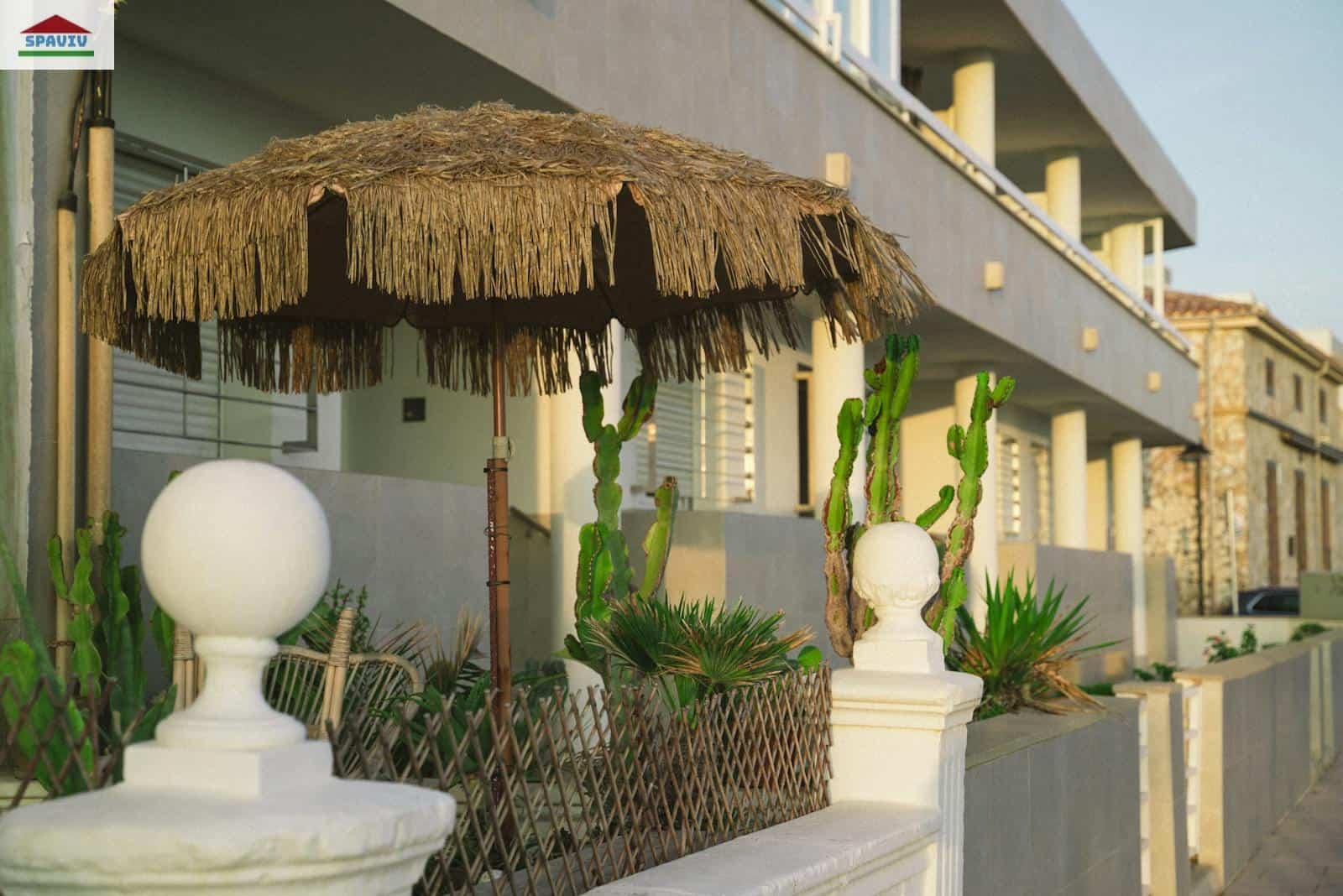 A stylish villa entrance with a straw parasol and cacti, evoking a tropical vibe.