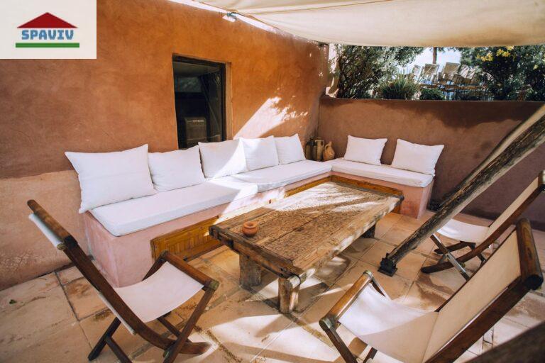 Inviting outdoor patio with rustic wooden furniture and white cushions, perfect for relaxation.